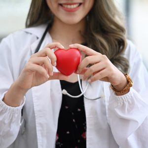 Smiling female doctor with stethoscope holding red heart. Cardiology concept.